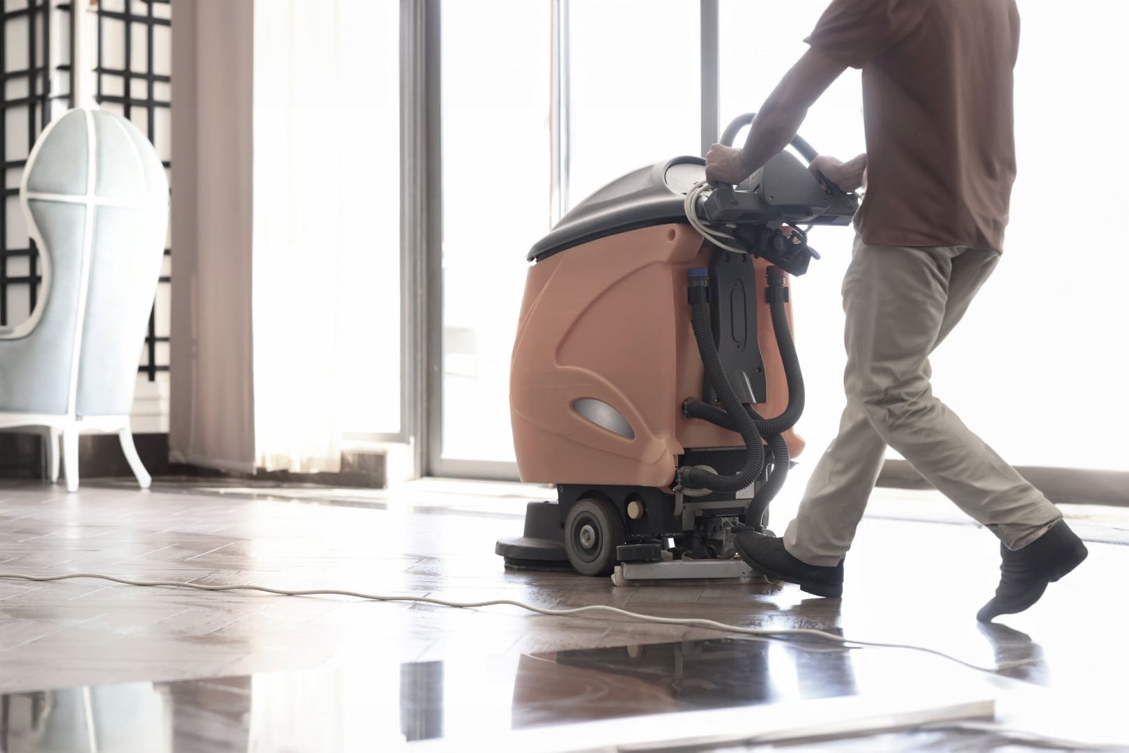 A man cleans the tiled floor with a wet vacuum cleaner