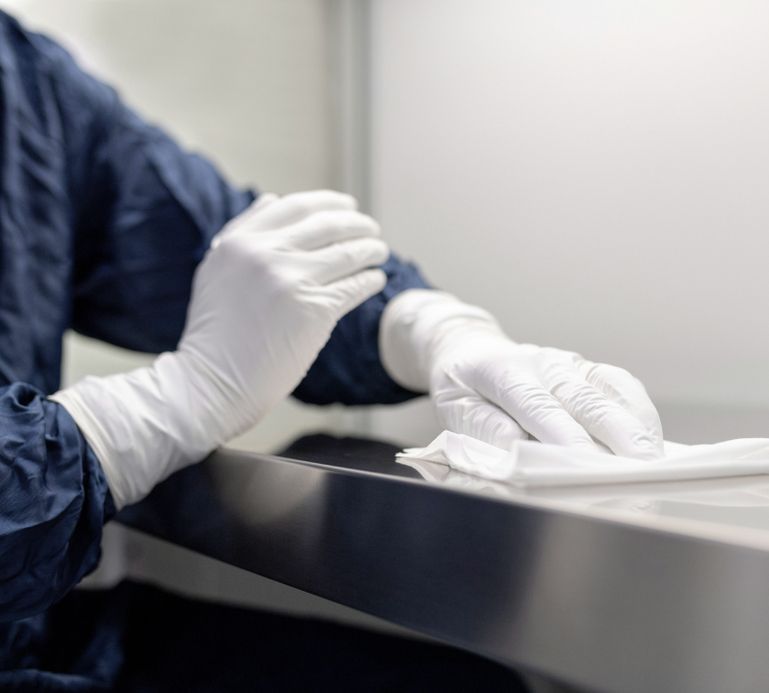 A person wearing blue overalls and white rubber gloves wipes the stainless steel surface with a cloth